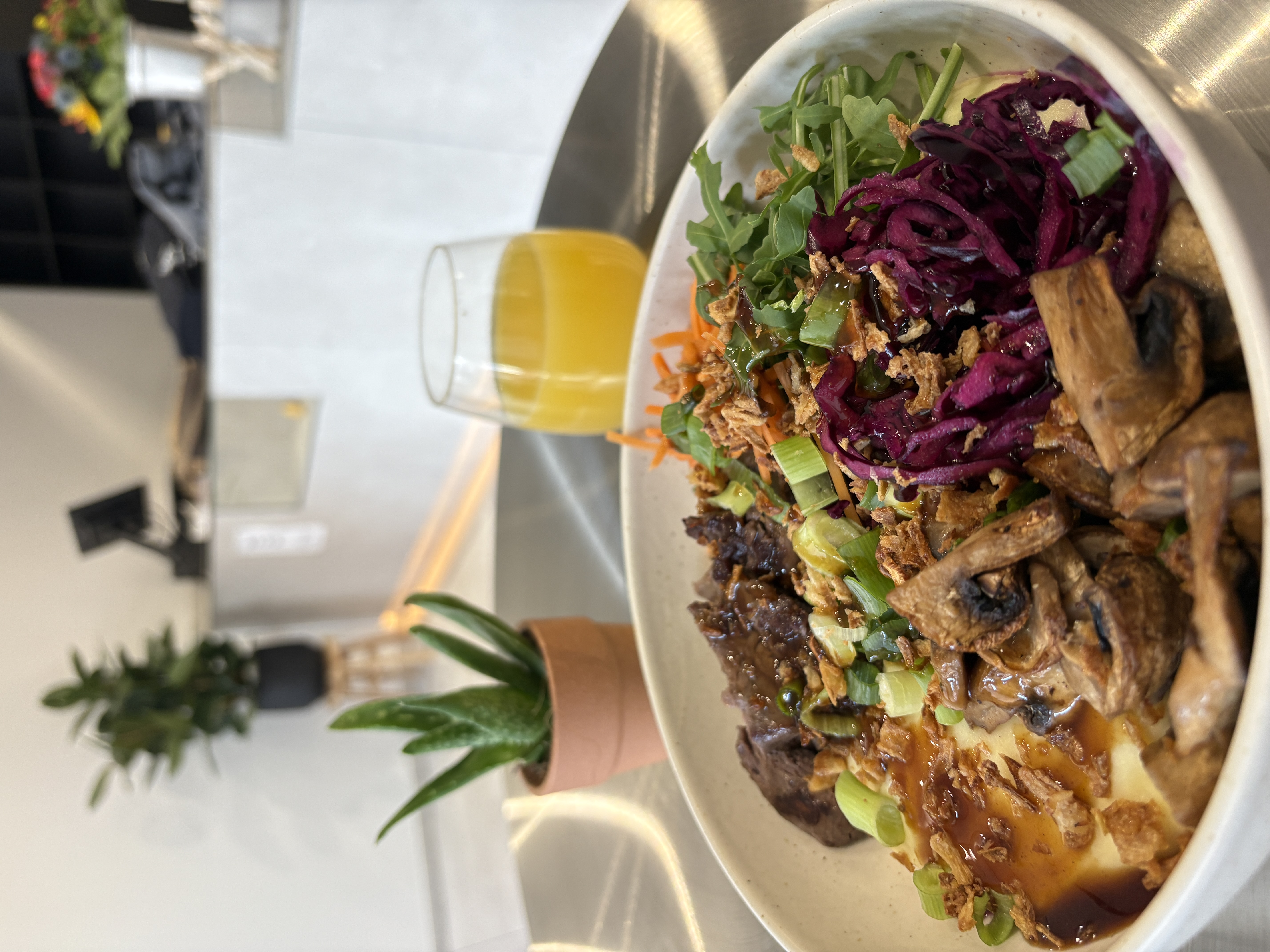 Hand holding a hamburger with lettuce, tomato, beef patty, mayonnaise, and sesame seed bun wrapped in paper against a red background.