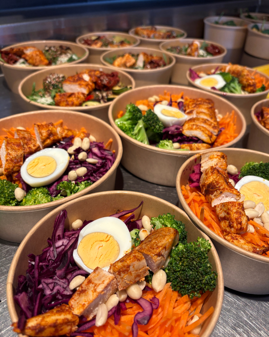 Smiling curly-haired woman with tattoos holding a sesame seed burger against a red background.